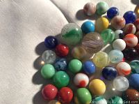 Close-up photo showing variety of colorful vintage glass marbles including swirled and solid colors on a white fabric.