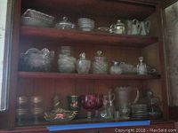 Three wooden shelves filled with assorted clear and colored glassware including pitchers, bowls, and small covered containers.