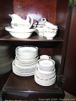 Full set stacked and displayed inside cabinet showing multiple plates, cups, and serving pieces with Dudley pattern.