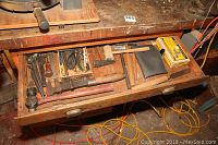 Open wooden drawer containing metal tools including hammers, wrenches, small hammer, pipe cutter, and boxes of nails.