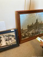 Two framed artworks side by side: one smaller black-framed photo of a fountain and paddle steamer, one larger wood framed print of Kingston Market Square with carriages.