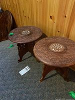 Two retro Indian themed carved wood tables with intricate floral carving and central circular inlay. Foldable carved legs visible. Moderate wear and patina visible.