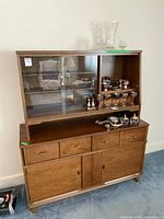 Full view of vintage wood buffet and hutch showing glass upper display shelves with silverware, four drawers and cupboards below.