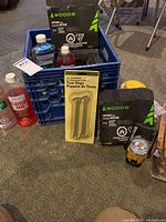 Overall photo showing blue crate with various camping supplies including boxed butane fuel packs, plastic bottles of lamp oil and packaged tent pegs.