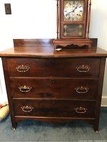 Front view of a dark wood 3-drawer chest of drawers with metal handles, showing wear and scratches.