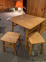 Full set showing wooden children's table and two stools on carpeted floor with wood-paneled walls in the background, visible surface scratches and fading on table top.