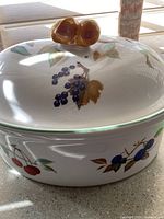 Photo showing entire covered casserole dish with fruit pattern and ceramic fruit-shaped lid handle, taken from above and side to highlight design and condition.