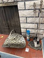 Fireplace tools with stand, wood holder with leopard print, and matches placed on a tiled hearth in front of fireplace screen