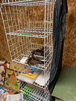 Side view of the white hanging wire rack showing three wire shelves with items placed on and around the shelves including garment bag hanging