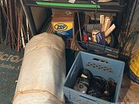 Photo showing large rolled white tarp, blue milk crate with extension cord reel, assorted painting supplies behind it, and box of Zep sweeping compound nearby.
