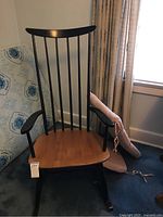 Front view of the Kennedy high back wooden rocking chair with black vertical slats and natural wood seat; carpet and window background visible.