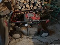 Side view of the Briggs & Stratton Craftsman push lawn mower showing front and rear wheels, handlebar, and overall condition near stacked firewood.