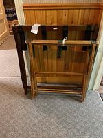 Two wooden luggage racks leaning against a wooden paneled wall. The racks have dark wood finish and black support straps.