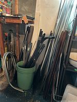 Green bucket filled with various metal rods and pipes, some bent and some straight, located against wall with additional rods leaning beside it.