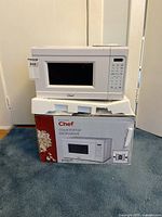 Front view of small white Master Chef microwave sitting on styrofoam packaging with original box underneath. Shows microwave door and window.