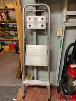 Front view of the closed aluminum two-step painting ladder standing upright.