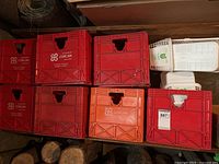 Seven red Corcan branded plastic crates, some showing bottom cracks, stacked on shelves along with white Foodland berry baskets on the right side.