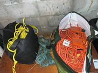 Bag holding yellow twisted rope and green thinner rope sitting next to a white bag containing orange extension cords.