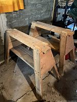 Pair of homemade wooden saw horses from front angle on concrete floor, showing top and legs construction details.