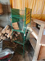 Front angled view of the green metal wire shelving unit with Schweppes-branded sign at the top, showing four basket shelves and overall shape.