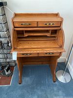 Front view of the wooden secretary desk with the roll top open, showing internal compartments and two top small drawers.