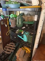 Black resin shelving unit with planting and gardening items on shelves for context, shelving dimensions approximately 35x13x55 inches.