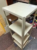 Four-shelf beige metal shelving unit in a basement or storage area, standing on a carpeted floor.