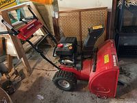 Front and side view of red Yard Machines snow blower with two small red jerrycans behind it