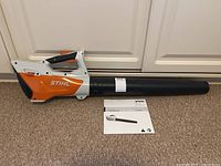 Full view of Stihl BGA 45 cordless leaf blower with owner's manual laid out in front on carpeted floor.