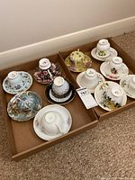 Photo showing 11 assorted vintage porcelain teacups and matching saucers in cardboard trays on carpet, brand marks visible on the bottom of cups and saucers