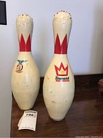 Two vintage Brunswick Two Score King bowling pins showing red crown logo and wear on plastic coating including scratches and cracks.