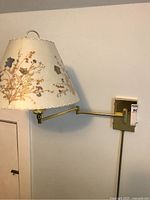 Full view of lamp mounted on wall showing cream floral Dornbusch lampshade and brass swing arm