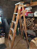 Full side view of the wooden folding step ladder standing open in a garage space with various items in background.