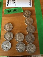 Ten Franklin half dollars on wood surface with green tape labeled ‘1961-1963’