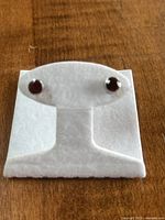 Photo of garnet stud earrings displayed on white padded holder showing size and setting