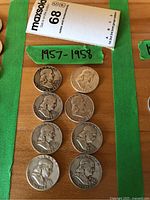Eight Franklin half dollars arranged on table with green tape label “1957-1958”