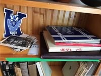 Wooden shelf with Kingston school yearbooks, postcards, and a felt letter patch leaning on the shelf wall.