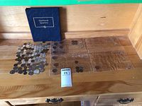 Coins and binder laid out on wooden surface. Binder labeled 'Statehood Quarters'. Multiple empty coin sleeves visible.