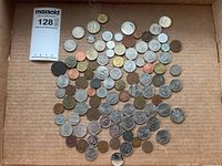 Top-down view of a large assortment of coins laid out in a cardboard box showing varied sizes, metals, and wear levels.