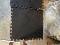 Black foam floor tiles laid on a surface next to a plastic bag containing more tiles, showing the puzzle-piece edges.
