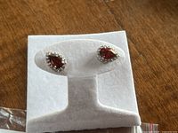 Pair of garnet and diamond teardrop earrings displayed on white earring stand.