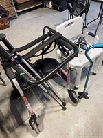 Overview showing rollator walker at front, shower chair behind, digital monitor on chair, teal quad cane at right.