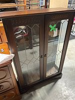 Front view of the oak curio cabinet with leaded glass doors, featuring a dark wood finish and two metal handles.