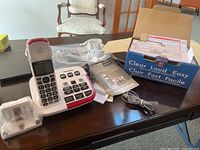 Full setup showing handset on base, original box, manuals, power adapter, and phone accessories.