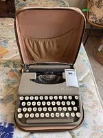 Small Smith-Corona Skyriter portable typewriter inside open beige carrying case on floral patterned surface.