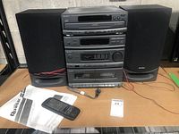 Complete Quasar Mini Changer System with two bookshelf speakers, remote control, owner's manual, and cables, arranged on a surface against a wall.