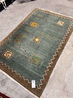 Full view of green mixed jewel tones floor rug with zigzag border and central motifs.