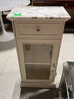 Front view showing drawer with metal knob and glass door with knob below, marble style top with slight discoloration.