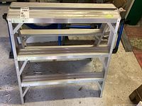 Front view of the aluminum step stool showing three wide steps and folding legs with grip lines on steps.