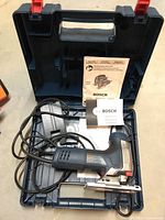 Full view of Bosch jigsaw inside open carrying case with manuals and blade